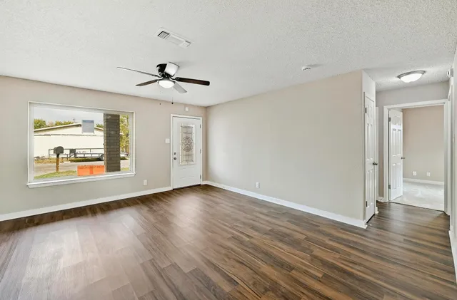 an empty room with wooden floor chandelier fan and windows