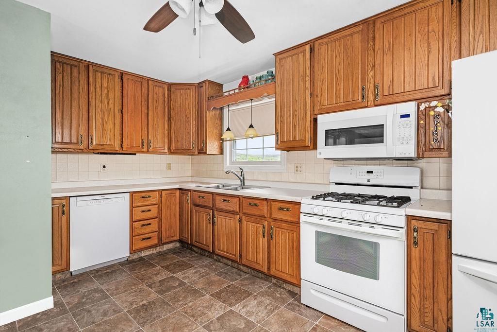 33 Nelson Drive Silver Bay, MN 55614 - Photo 11 of 40 Kitchen with white appliances, a sink, brown cabinetry, decorative backsplash, and light countertops