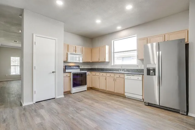 a kitchen with granite countertop a refrigerator oven a sink and white cabinets