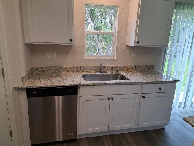 a kitchen with granite countertop white cabinets sink and window
