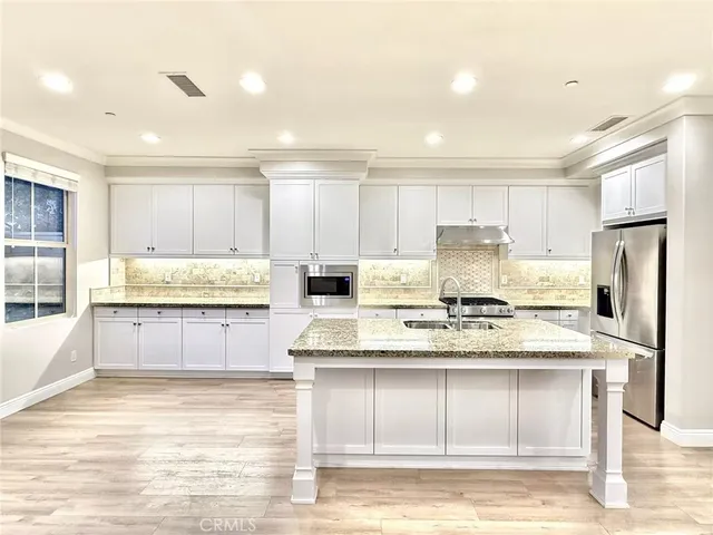 a large kitchen with kitchen island granite countertop a stove a sink a refrigerator and white cabinets