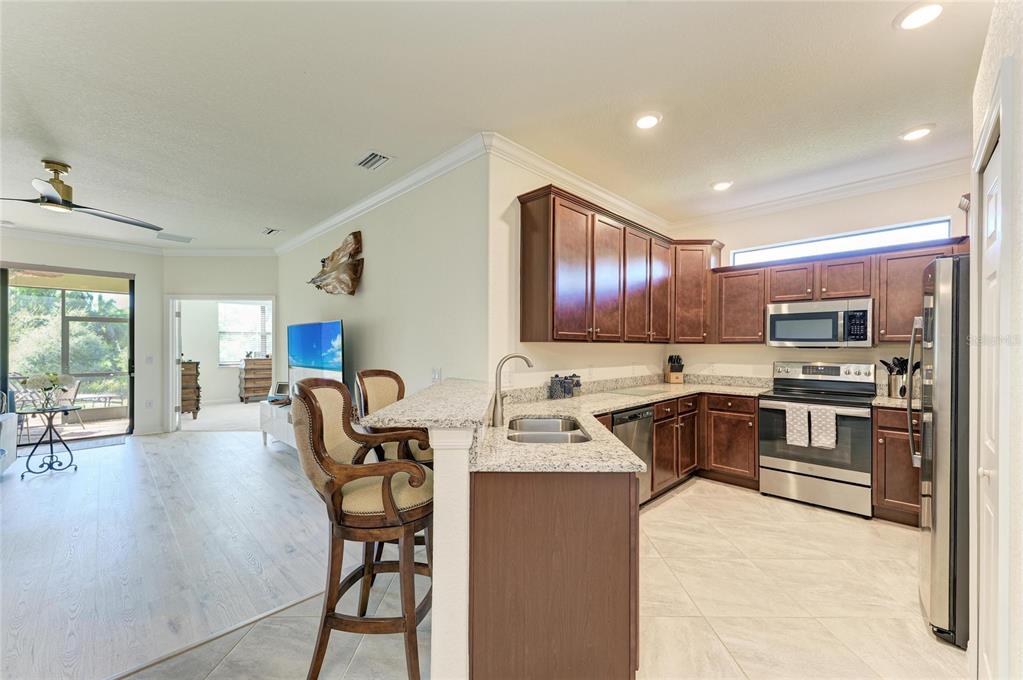 12440 Amica Loop Venice, FL 34293 - Photo 26 of 87 a kitchen with stainless steel appliances granite countertop a stove top oven a sink dishwasher a dining table and chairs with wooden floor