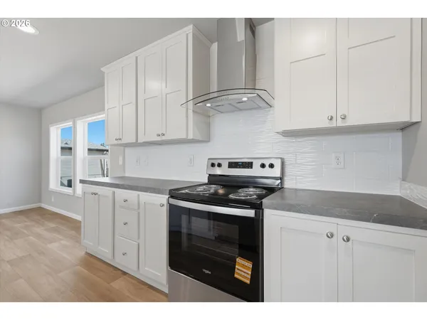 a kitchen with stainless steel appliances granite countertop a sink stove and white cabinets with wooden floor