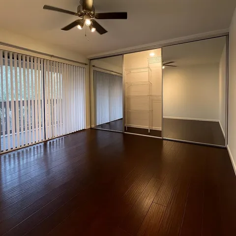 an empty room with wooden floor fan and windows
