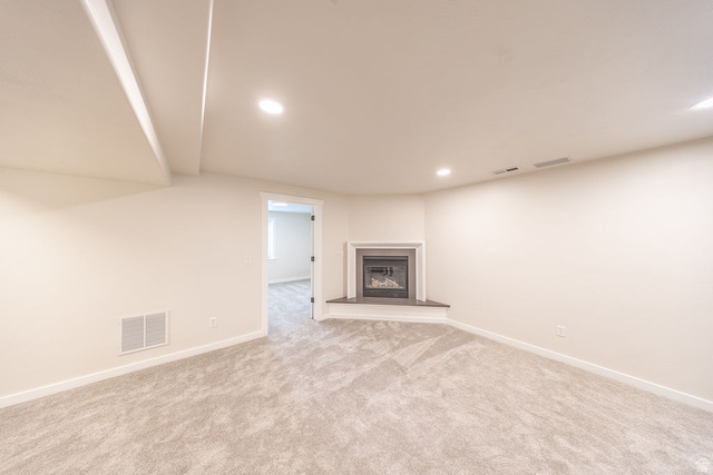 2169 Orchard Pines Loop East Bountiful, UT 84010 - Photo 25 of 32 Spacious room featuring a corner fireplace with a dark surround and hearth, neutral-toned carpet, recessed lighting, and white baseboards