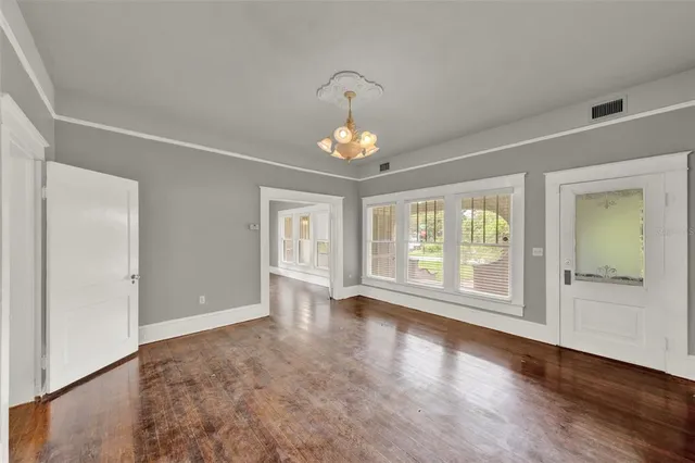 an empty room with wooden floor chandelier and windows