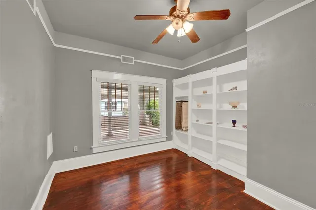 an empty room with wooden floor chandelier fan and windows