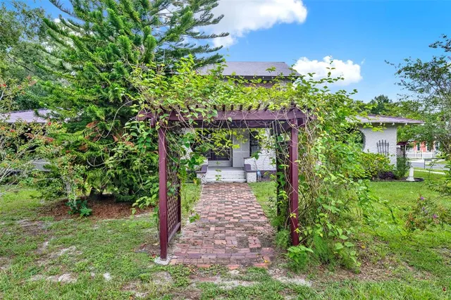 a pathway of a house with potted plants and large trees