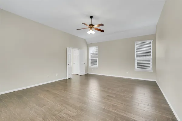 an empty room with wooden floor ceiling fan and window