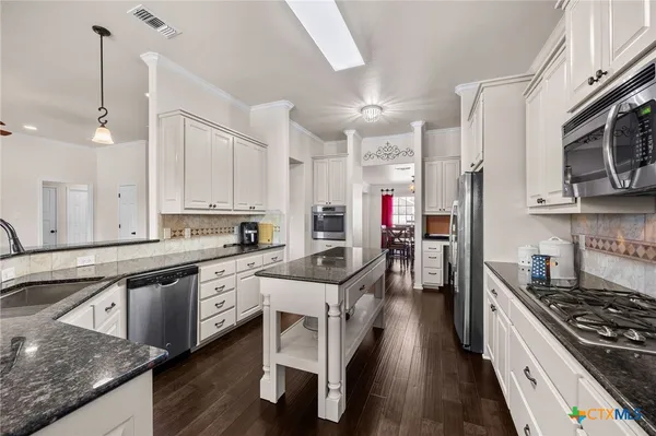 a kitchen with stainless steel appliances granite countertop a stove top oven a sink dishwasher and white cabinets with wooden floor