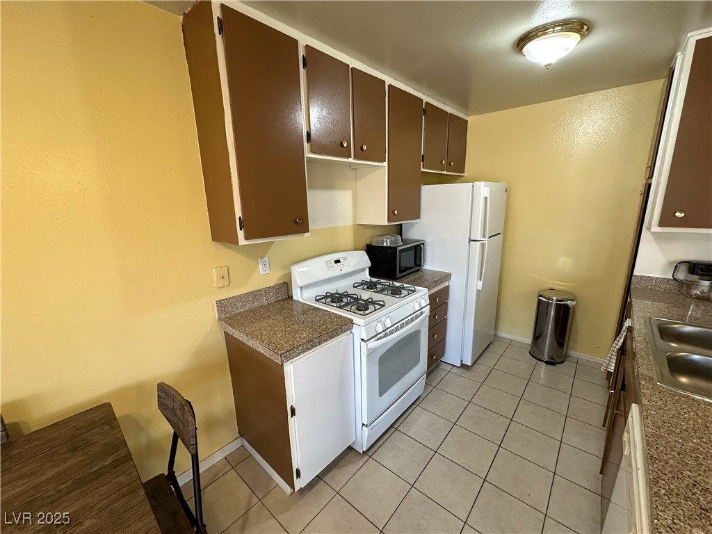 3936 Rive Gauche Street Las Vegas, NV 89115 - Photo 15 of 30 Kitchen featuring white appliances, dark countertops, light tile patterned floors, baseboards, and a sink
