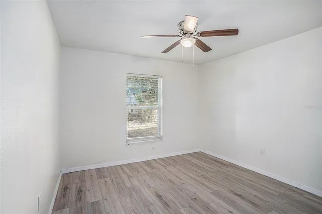 an empty room with wooden floor fan and windows