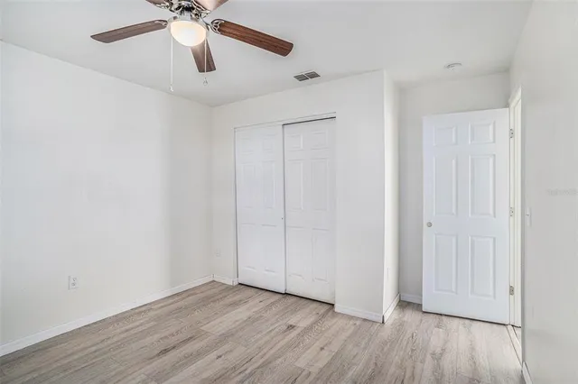an empty room with wooden floor fan and windows