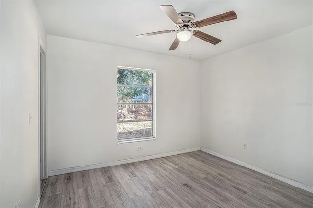 an empty room with wooden floor ceiling fan and window
