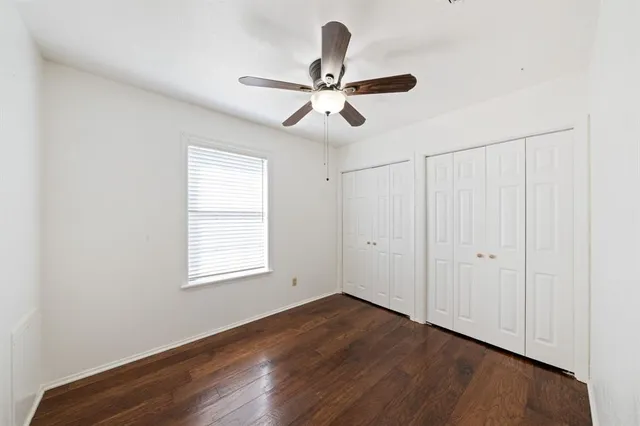 an empty room with wooden floor ceiling fan and windows