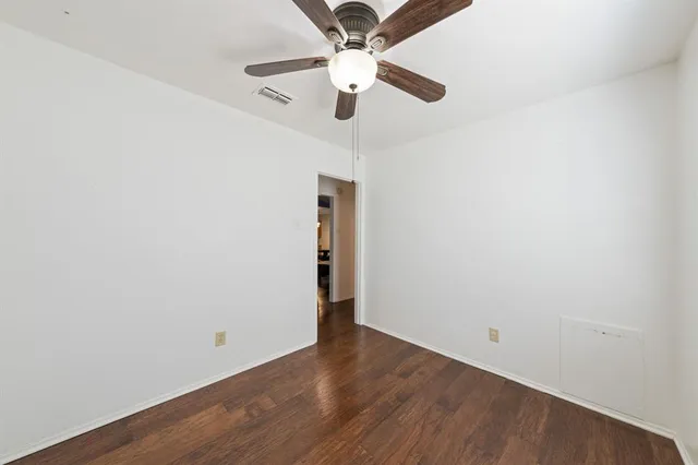an empty room with wooden floor ceiling fan and window