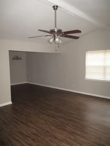 an empty room with wooden floor windows and fan