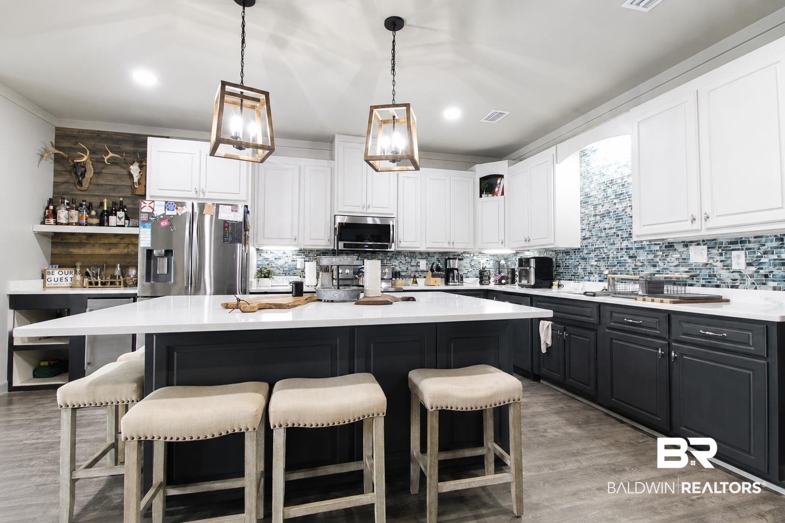 9825 Wolf Creek Ridge Elberta, AL 36530 - Photo 34 of 76 Contemporary kitchen featuring a large central island with a solid surface countertop, two-tone cabinetry with white upper and dark lower units, a full-height blue and white mosaic tile backsplash, wood-finish flooring, and two wood-framed pendant lights