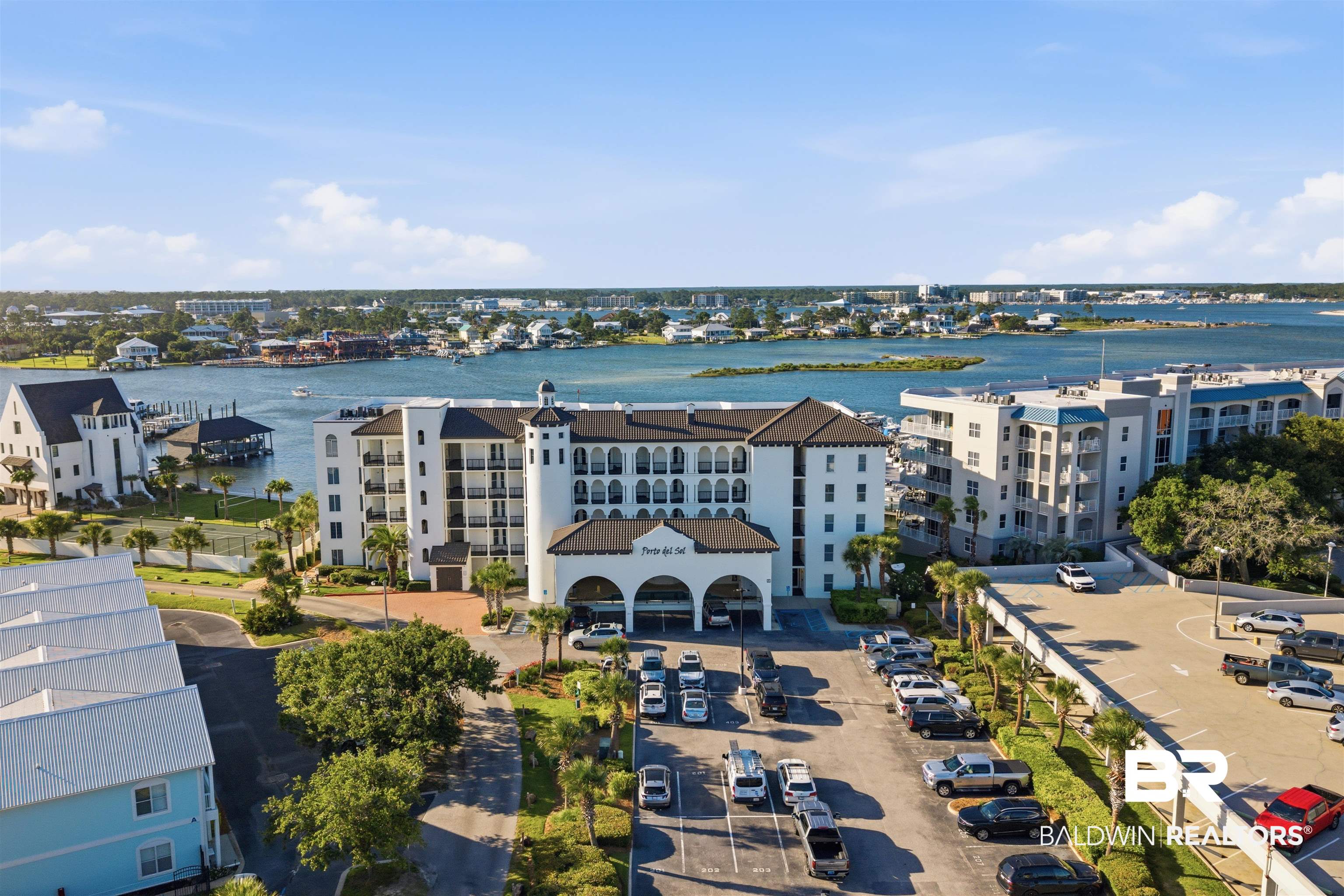 3564 Bayou Road, Unit 203 Orange Beach, AL 36561 - Photo 46 of 53 Waterfront condominium building featuring a multi-level parking structure, covered entry archway, balconies on upper levels, and surrounding mature palm trees