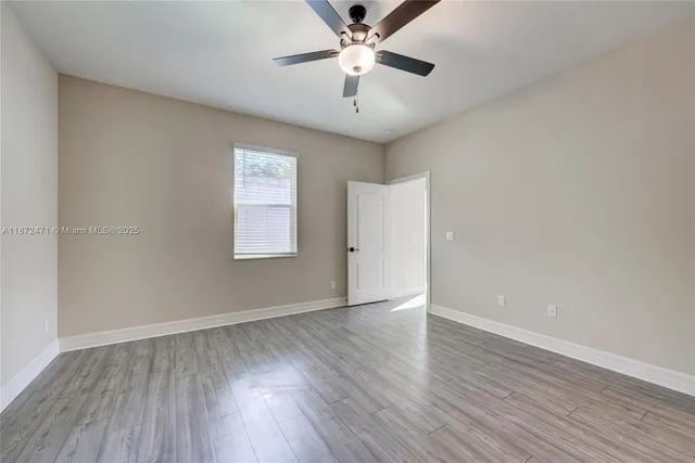 an empty room with wooden floor chandelier fan and windows