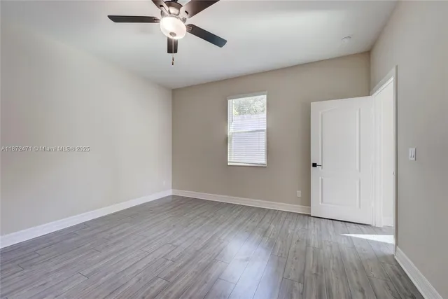 an empty room with wooden floor chandelier fan and windows