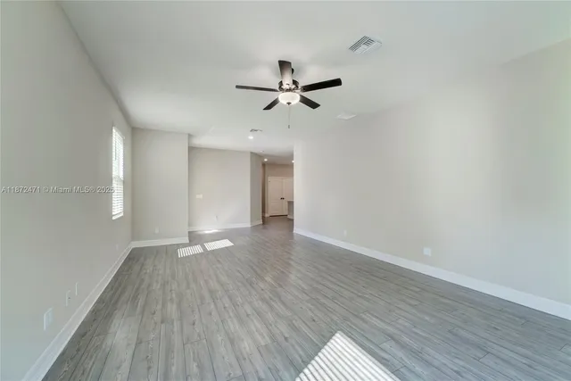 an empty room with wooden floor ceiling fan and windows