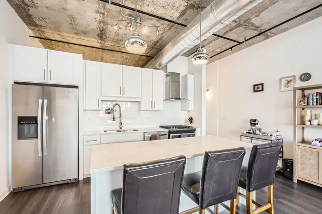 a kitchen with stainless steel appliances kitchen island granite countertop a refrigerator a sink dishwasher and white cabinets with wooden floor