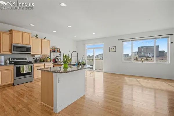 a kitchen with stainless steel appliances a microwave a stove a sink dishwasher a refrigerator and a dining table with wooden floor