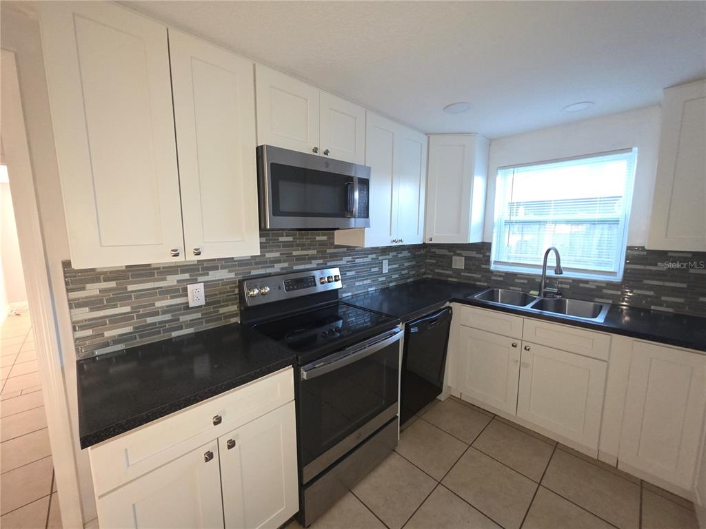 1344 Wickham Lane Holiday, FL 34691 - Photo 5 of 17 a kitchen with granite countertop white cabinets and black appliances