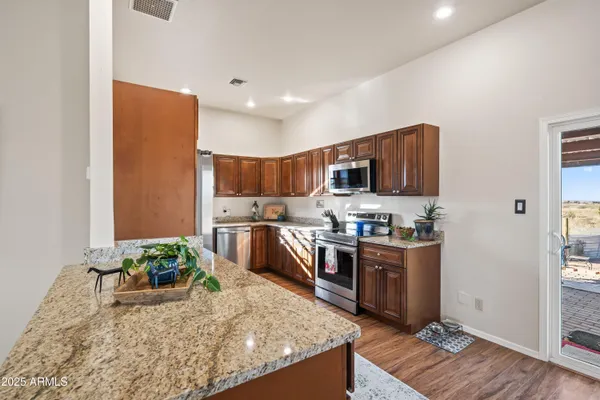 a kitchen with stainless steel appliances granite countertop a stove top oven a sink dishwasher and a refrigerator with wooden floor