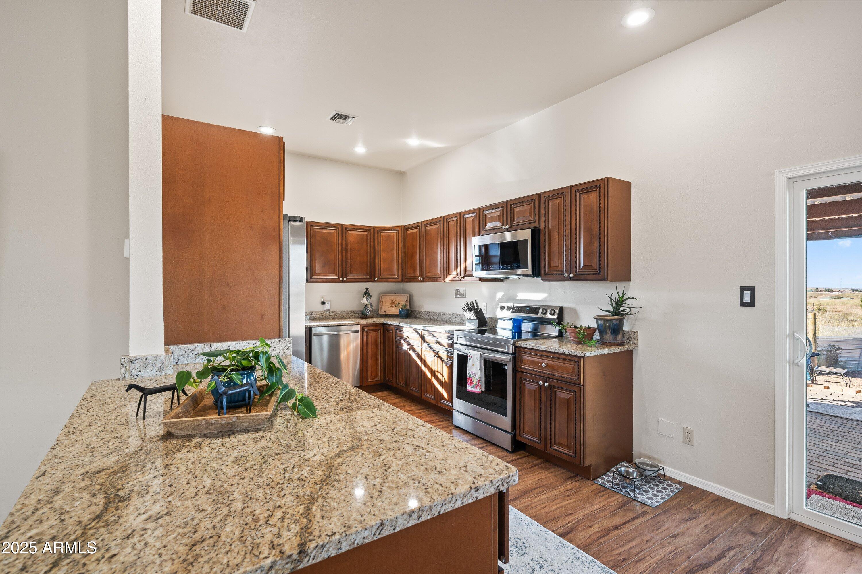 105 Los Encinos Road Sonoita, AZ 85637 - Photo 11 of 39 a kitchen with stainless steel appliances granite countertop a stove top oven a sink dishwasher and a refrigerator with wooden floor