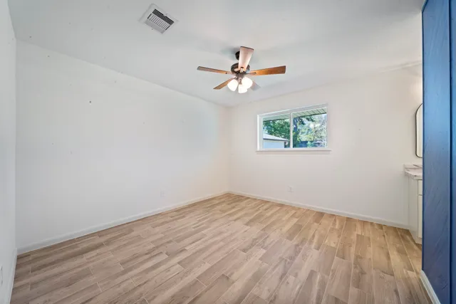 an empty room with wooden floor ceiling fan and window