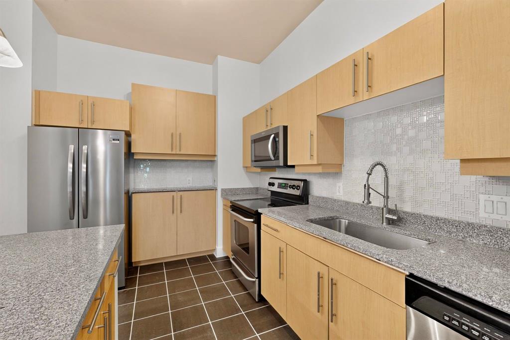 Kitchen featuring light wood-finish cabinetry, stainless steel appliances, granite countertops, and a mosaic tile backsplash