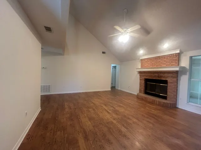 an empty room with wooden floor fireplace and windows