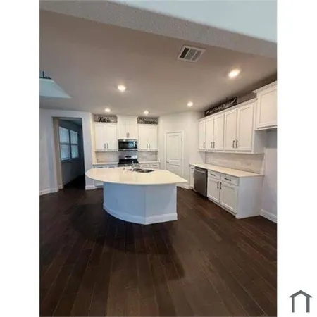 a large kitchen with kitchen island a sink dishwasher a stove a refrigerator with white cabinets and wooden floor