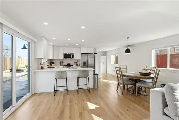 a kitchen with stainless steel appliances kitchen island granite countertop a dining table chairs and a refrigerator