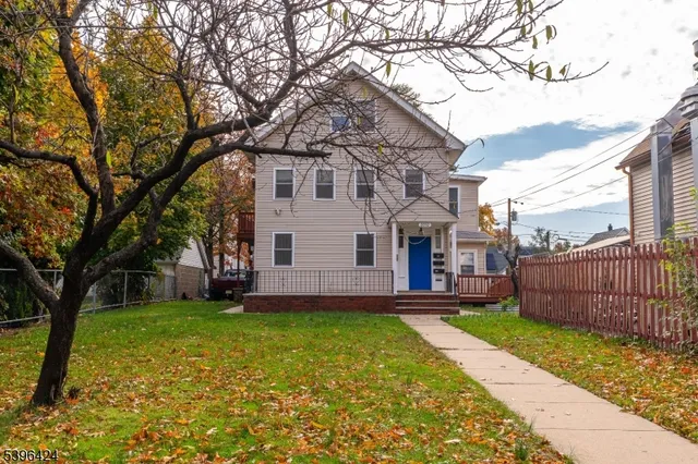 a view of a white house next to a yard and a large tree