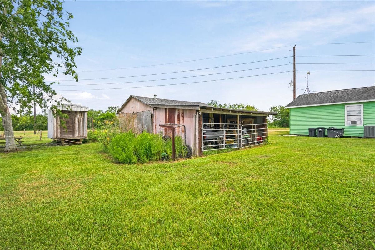 765 Norcross Road Wallis, TX 77485 - Photo 36 of 42 This photo shows a spacious backyard with a well-maintained lawn, featuring a small wooden shed and a larger structure for storage or livestock.