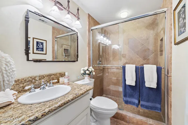 a bathroom with a granite countertop sink a toilet a mirror and shower