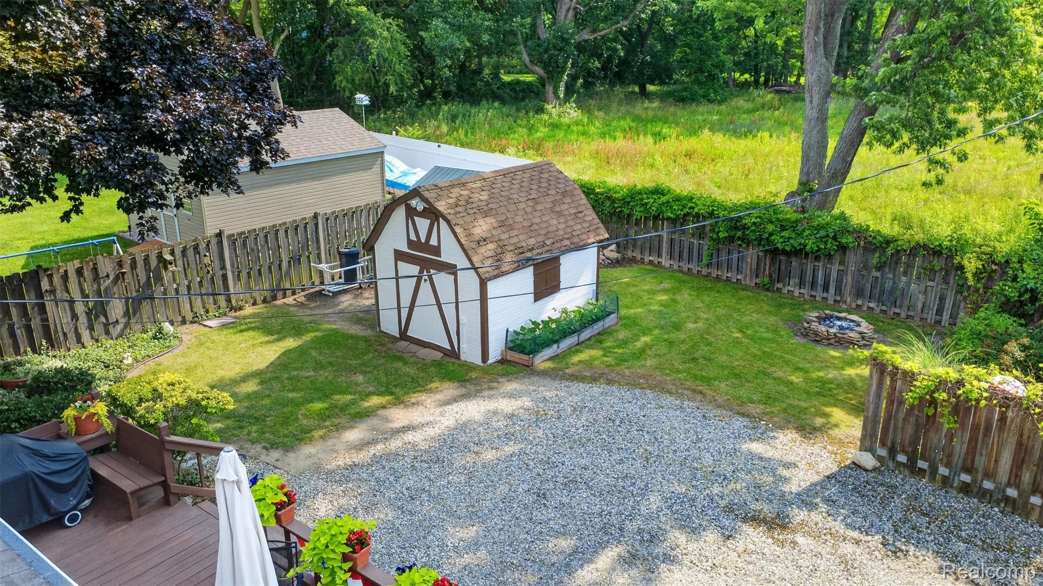 5977 Anglers Road Ortonville, MI 48462 - Photo 41 of 63 Expansive backyard featuring a gravel patio, wood-finish deck, fencing, a barn-style storage shed, and a stone fire pit