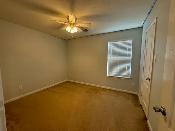 an empty room with a chandelier fan and windows
