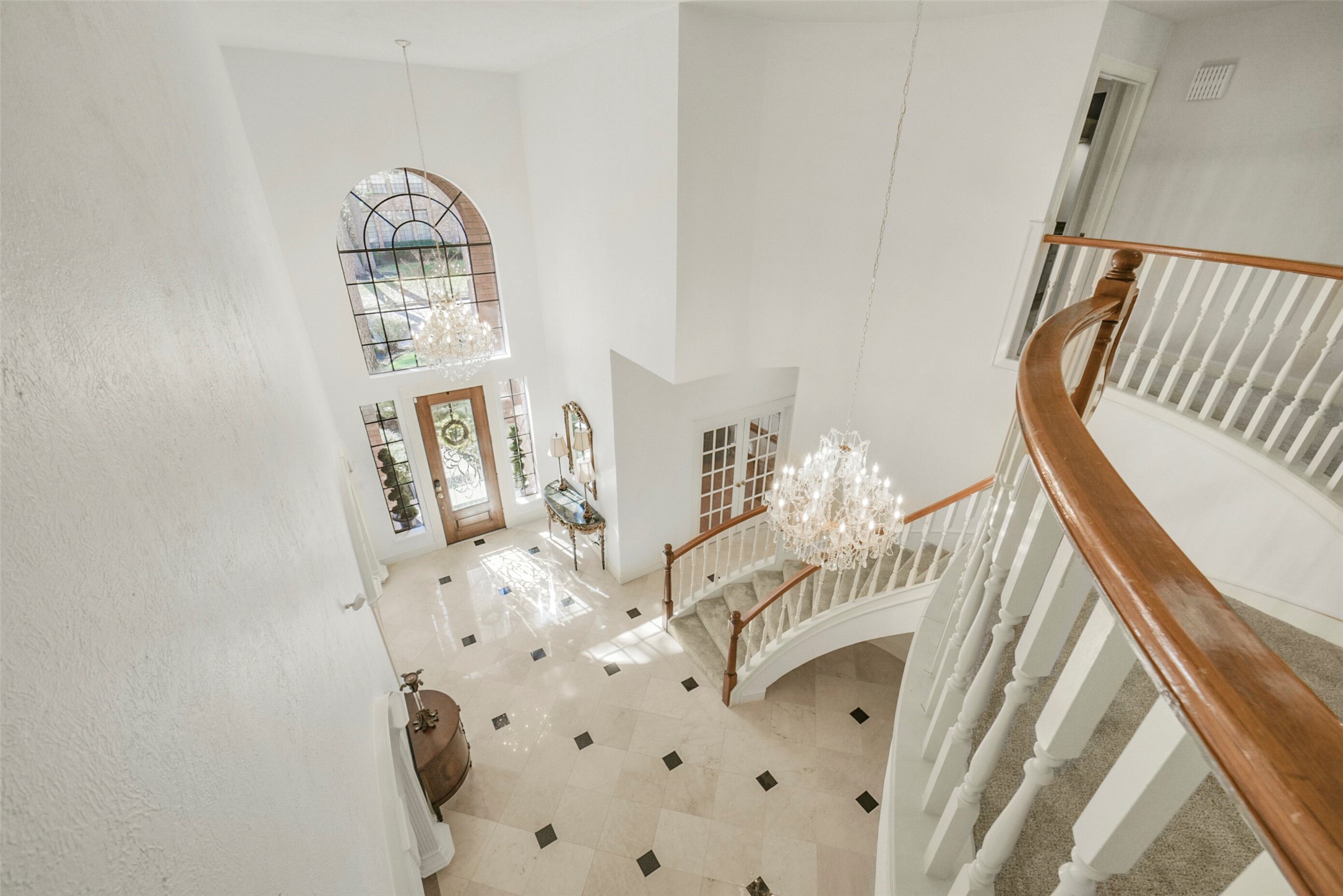 17302 Atherington Place Spring, TX 77379 - Photo 31 of 50 This captivating photo captures the essence of the property's grandeur, showcasing a breathtaking view from the balcony. The image highlights the stunning entry area, adorned with exquisite chandeliers that illuminate the space with warm, inviting light. The focal point is undoubtedly the elegantly curved staircase, a true architectural masterpiece that beckons you to explore the home's interior.