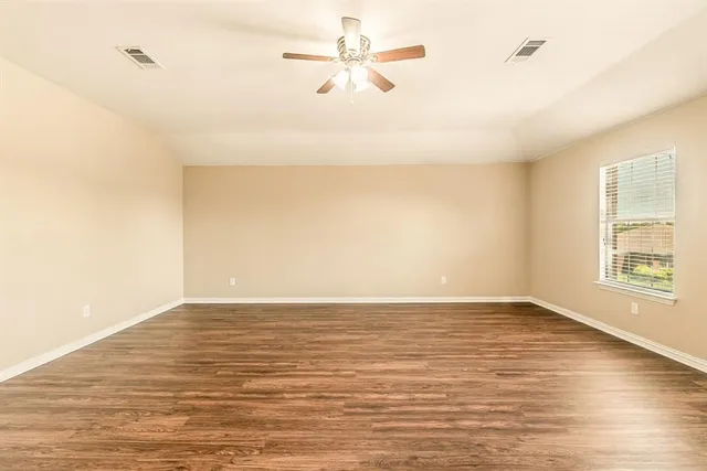 an empty room with wooden floor and a ceiling fan