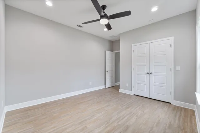 an empty room with wooden floor ceiling fan and windows