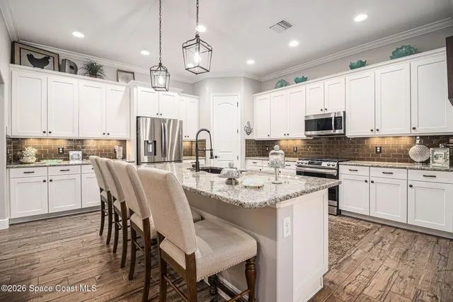 a kitchen with stainless steel appliances kitchen island granite countertop a table chairs sink and cabinets