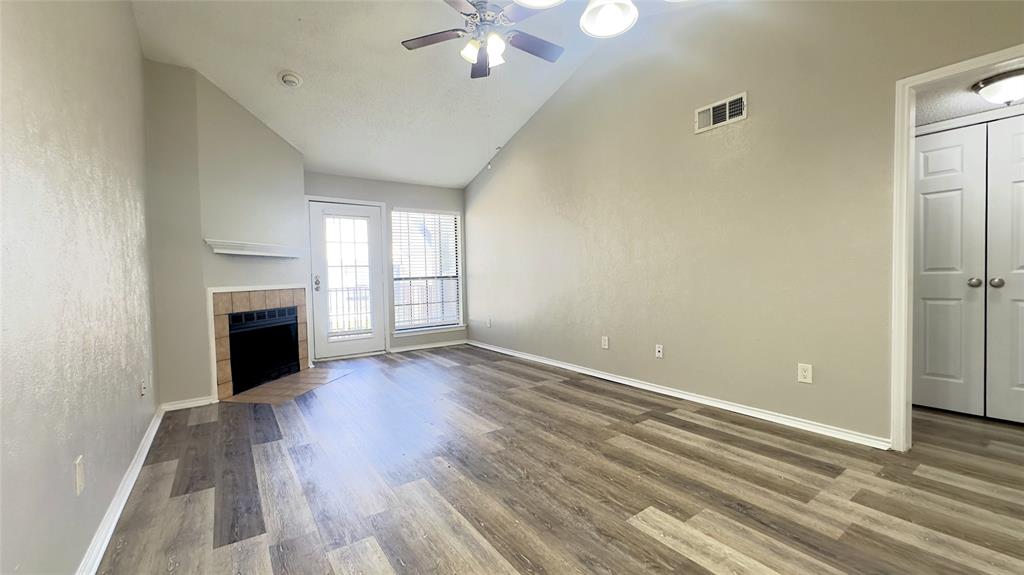 9601 Forest Lane, Unit 323 Dallas, TX 75243 - Photo 4 of 23 Unfurnished living room with dark wood-style floors, a fireplace, ceiling fan, high vaulted ceiling, and a textured wall