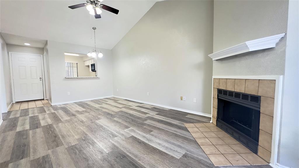 9601 Forest Lane, Unit 323 Dallas, TX 75243 - Photo 5 of 23 Unfurnished living room with a fireplace, high vaulted ceiling, light wood finished floors, ceiling fan, and a chandelier