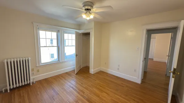 an empty room with wooden floor fan and windows