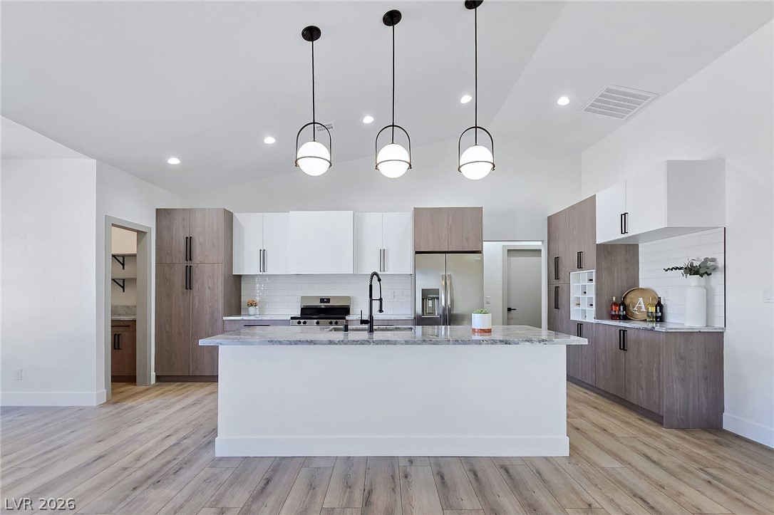 1120 West Gamebird Road Pahrump, NV 89048 - Photo 14 of 36 Kitchen with tasteful backsplash, hanging light fixtures, brown cabinetry, light stone countertops, and stainless steel appliances