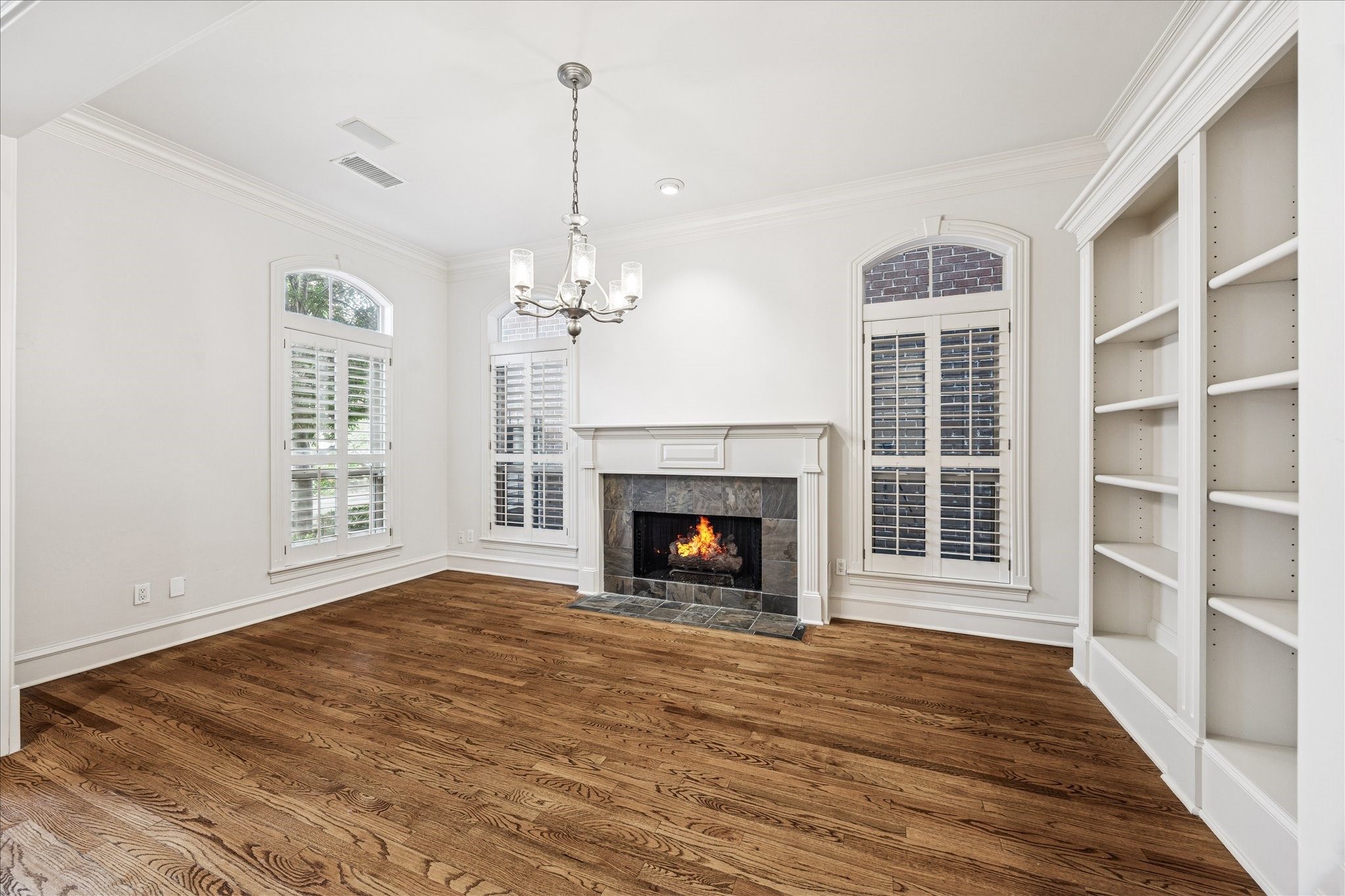 5823 Augusta Court Houston, TX 77057 - Photo 5 of 44 The Living Room features hardwood floors, a cozy fireplace, and built-in shelving. It has large arched windows with shutters, providing ample natural light, and a stylish chandelier enhances the elegant atmosphere.
